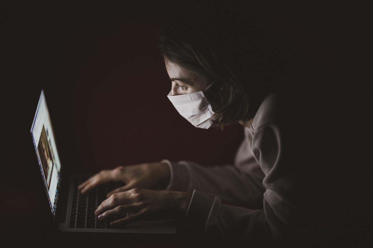 Person wearing a mask, using a laptop in the dark.